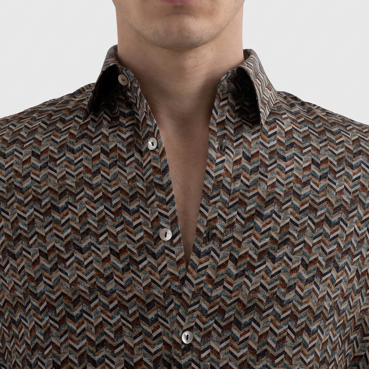A man wearing a long-sleeve button-down shirt with a brown, beige, and black chevron pattern, shown from the chest up against a light gray background.