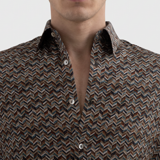 A man wearing a long-sleeve button-down shirt with a brown, beige, and black chevron pattern, shown from the chest up against a light gray background.