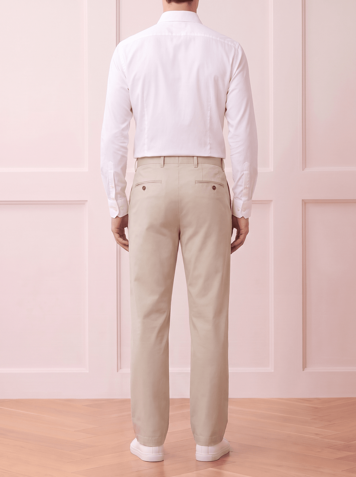 A man viewed from behind wearing a Beige long-sleeve button-up shirt and light beige trousers, standing against a white textured wall.
