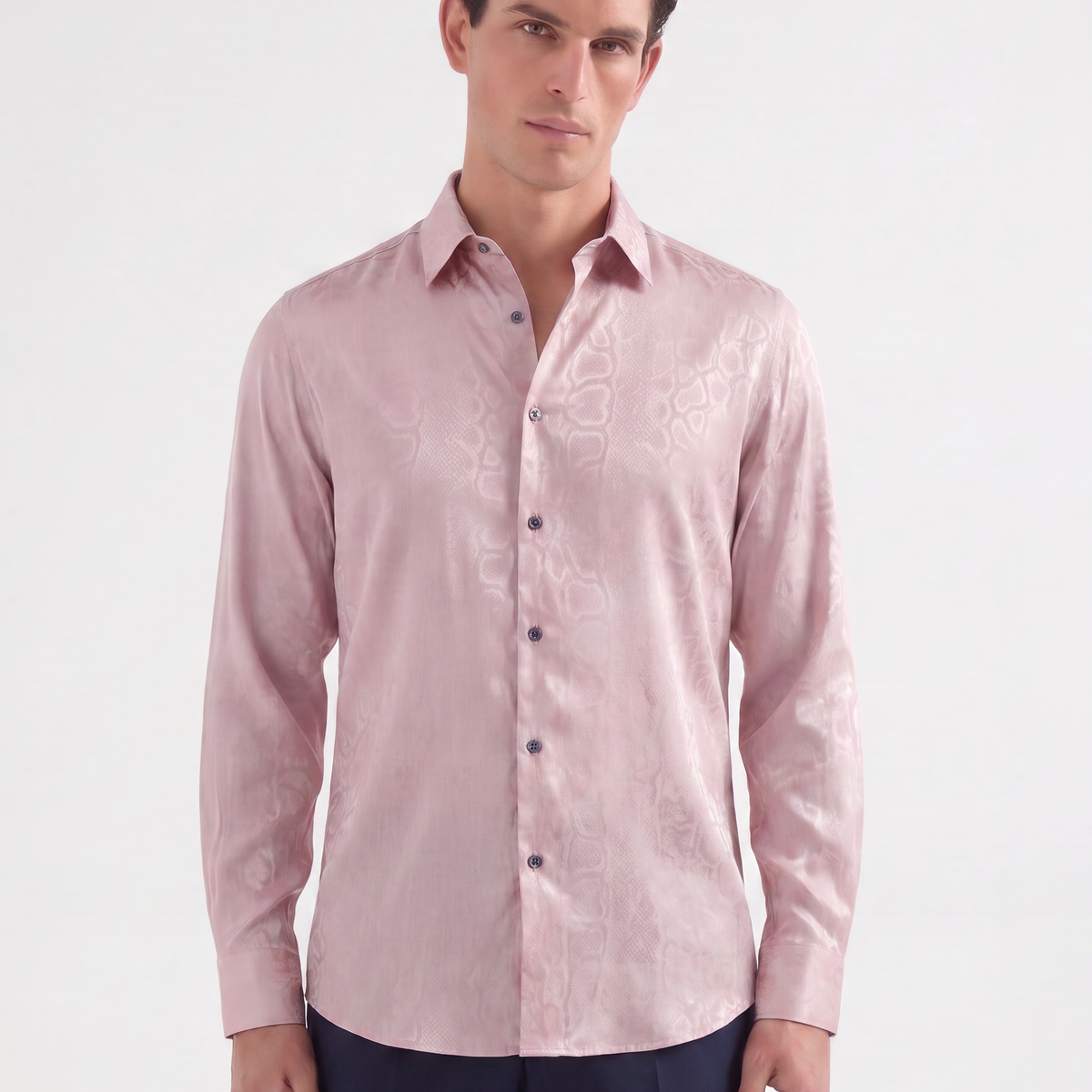 A man wearing a light pink long-sleeve button-up shirt with a subtle tonal floral jacquard pattern, paired with navy trousers, against a plain white studio background.