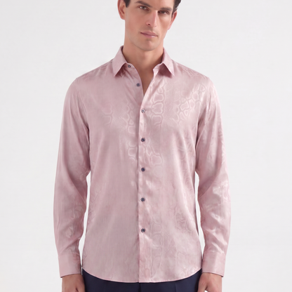 A man wearing a light pink long-sleeve button-up shirt with a subtle tonal floral jacquard pattern, paired with navy trousers, against a plain white studio background.