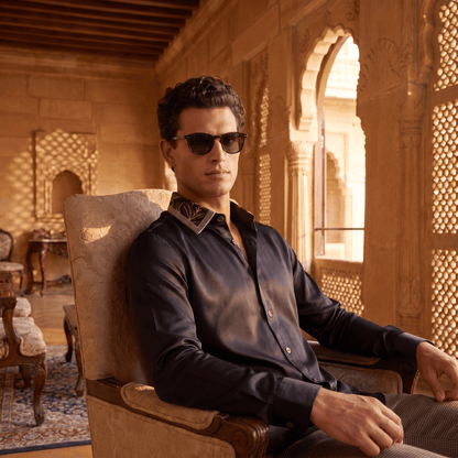 Embroidered black linen-satin shirt with floral collar on man in ornate setting